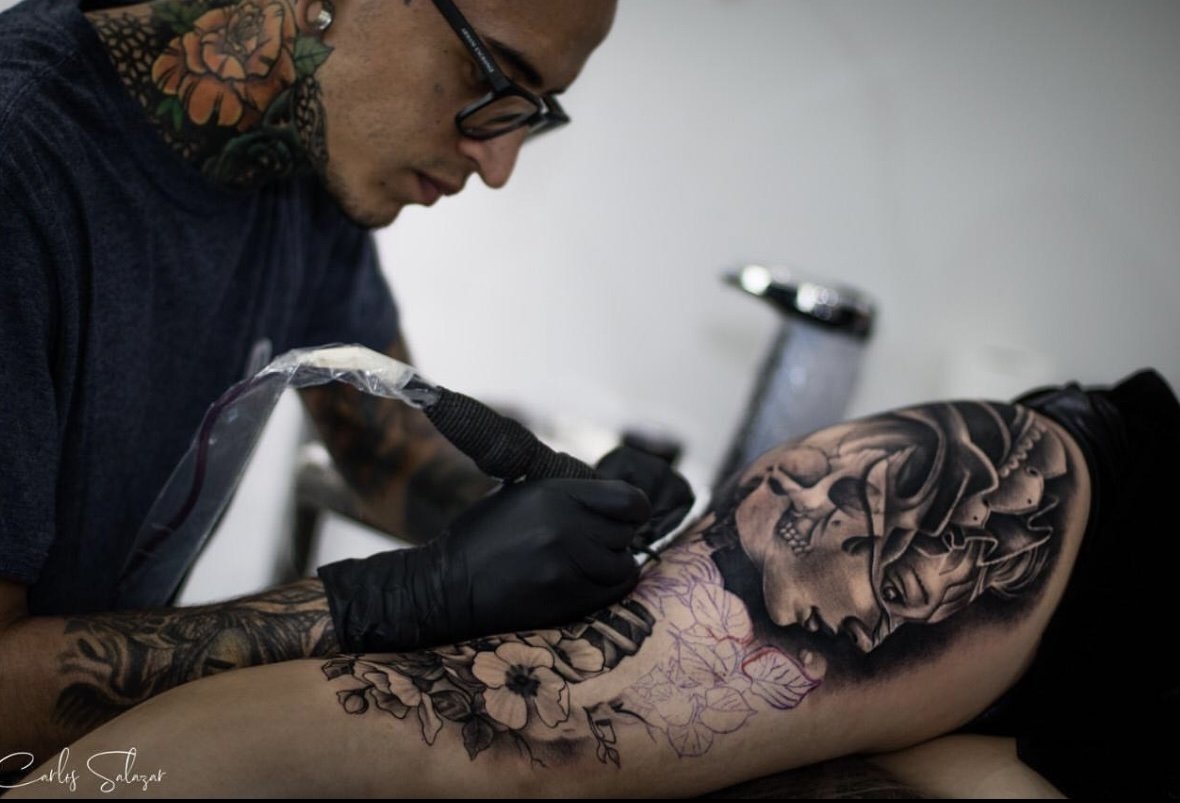 Tatuador realizando un tatuaje black and grey de rostro femenino, calavera y flores en Cali Tattoo Festival 2019