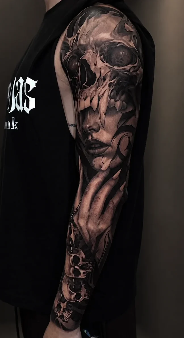Tatuaje black and grey de calavera y rostro femenino en brazo